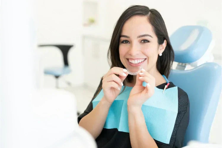 Une femme dans un cabinet de dentiste, tenant un aligneur et souriante.