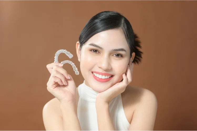 une belle femme aux traits symétriques tenant des aligneurs transparents