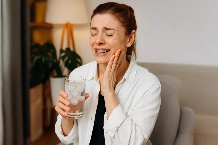 A woman suffering from braces pain while holding a glass full of ice water